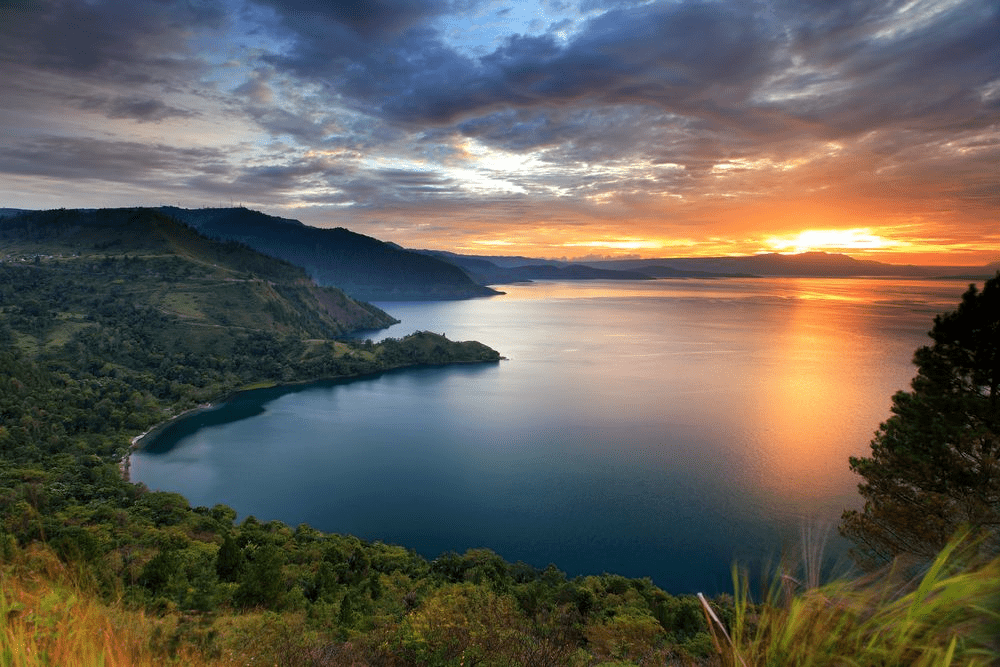 Early morning mist rising over the still water of Lake Toba, creating a serene, peaceful atmosphere.